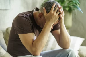 Man sitting on couch with head in hands with a flat, numb expression as grief quietly deepens into depression